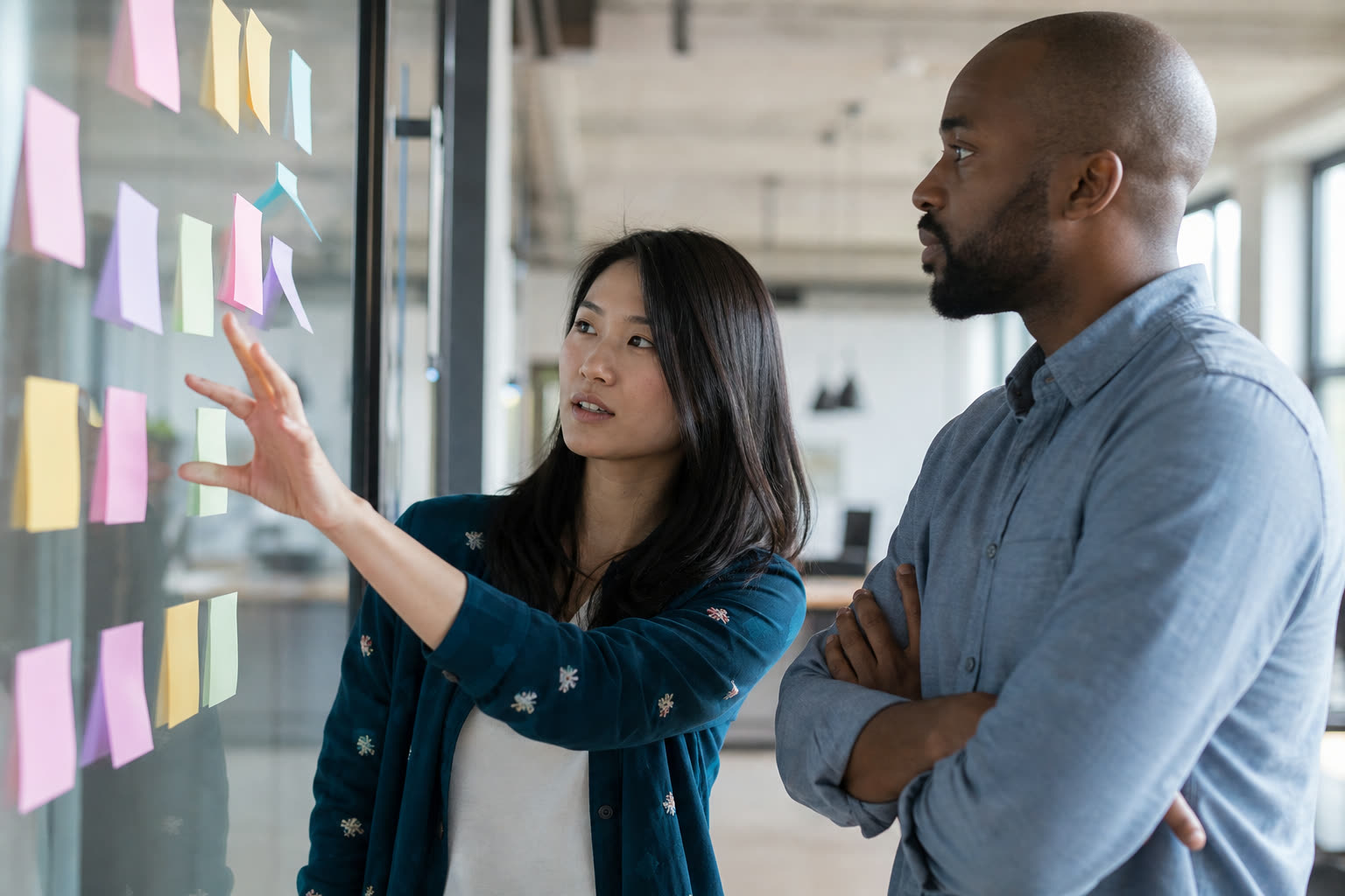Two colleagues mapping a process together on a glass wall covered with blank sticky notes.